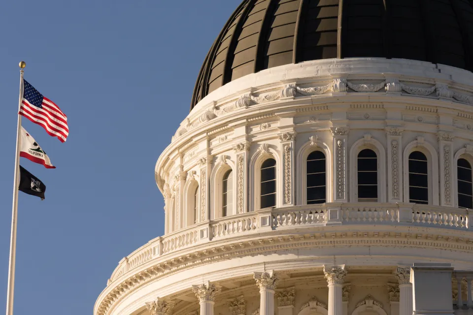 Close-up of Californis state capitol dome with U.S., California, and POW/MIA flags on flagpole.